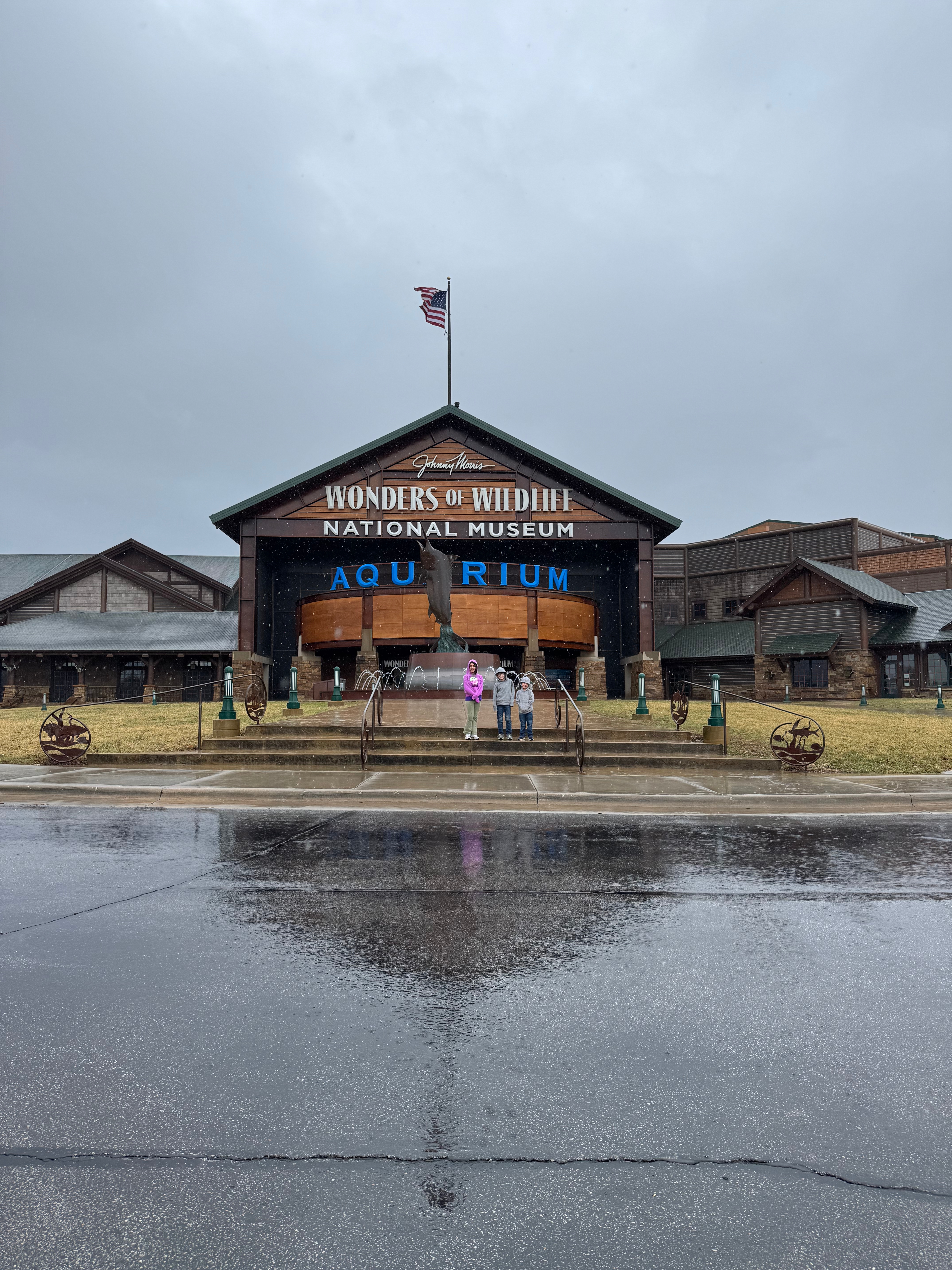 Family standing in front of the Wonders of Wildlife National Museum and Aquarium in Springfield, Missouri, on a rainy day.